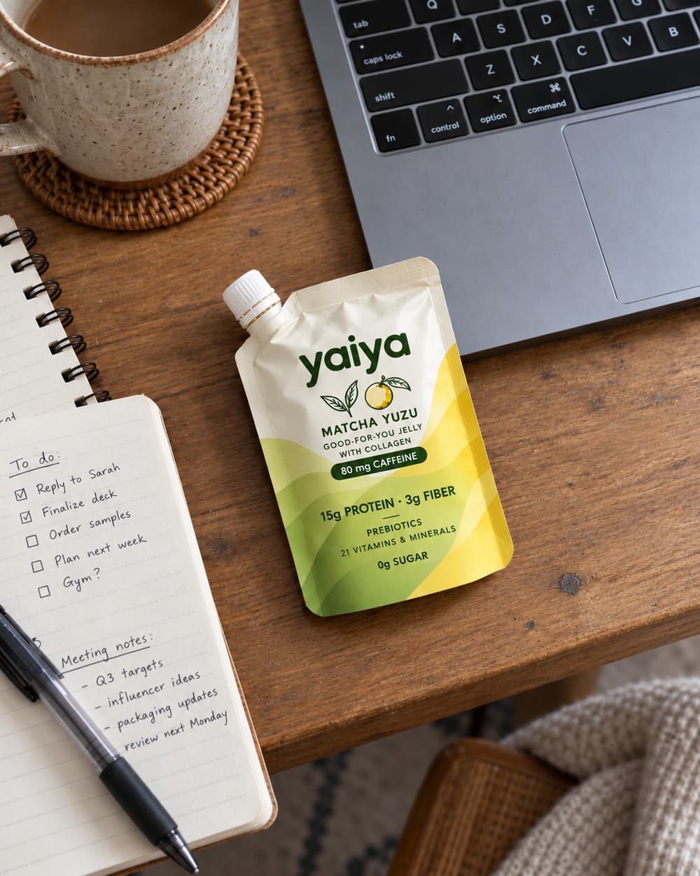 A Matcha Yuzu pouch on a wooden desk beside a laptop, a mug of coffee and a notebook with a to-do list.