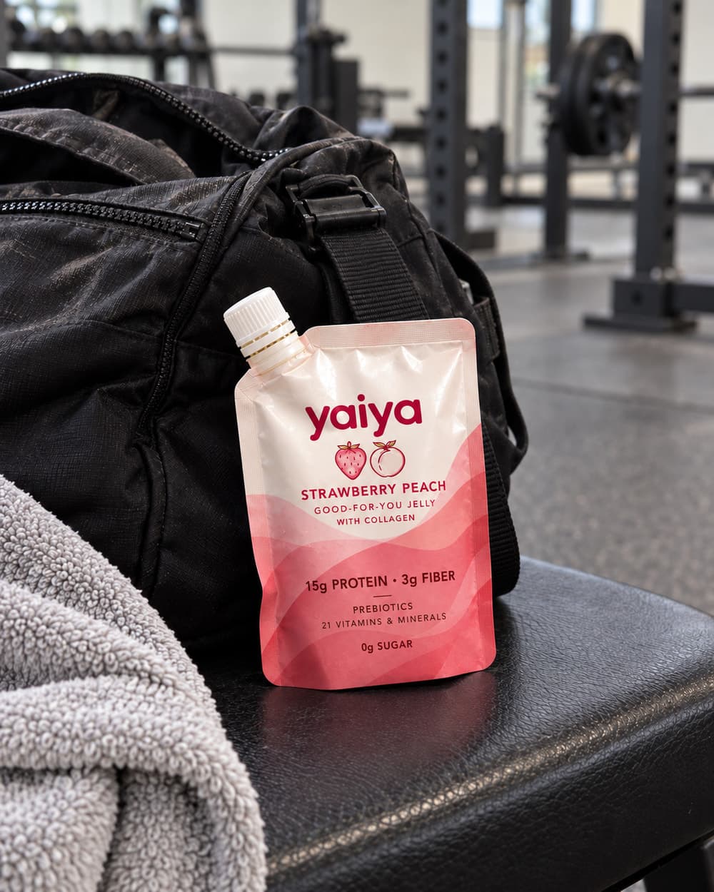 A Strawberry Peach pouch on a gym bench, leaning on a black gym bag beside a towel, with weight racks behind.